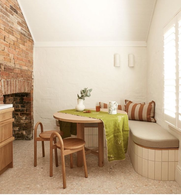 a kitchen table with two chairs and a bench next to it in front of a brick wall