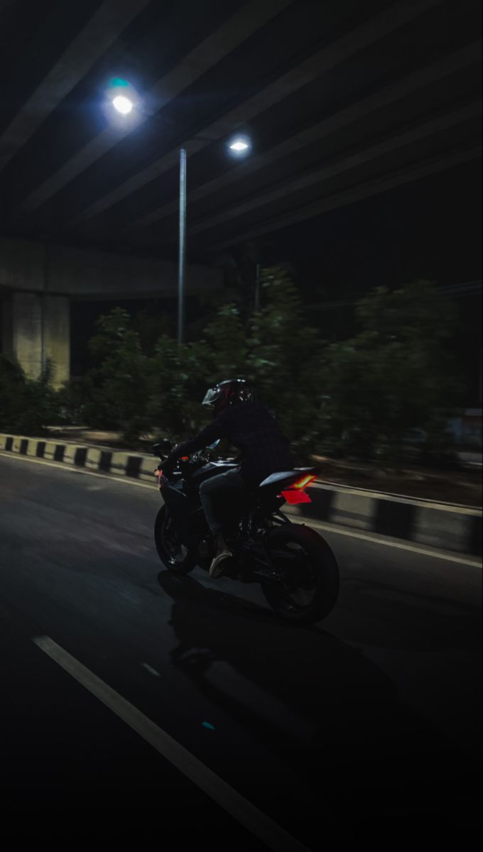 a man riding a motorcycle down a street at night with the lights on and trees in the background