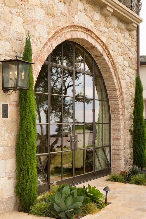 an arched window is shown in front of a stone building with potted plants and greenery