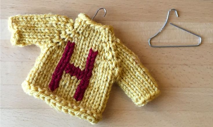 a knitted sweater with the letter h on it next to a pair of hooks