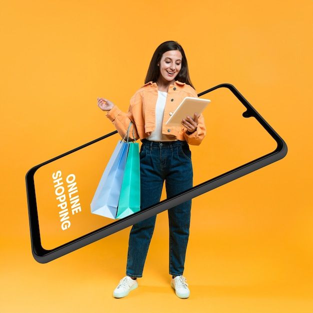 a woman holding shopping bags and looking at her cell phone while standing in front of an orange background