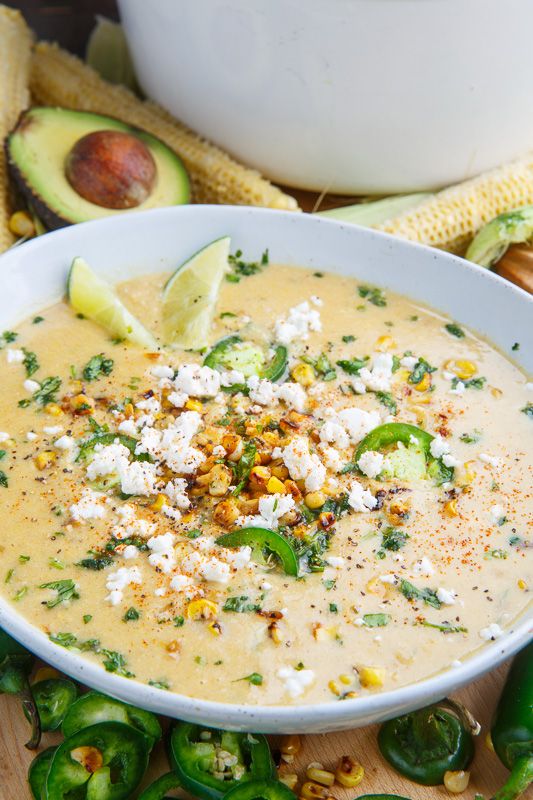 a white bowl filled with soup next to green peppers and corn on the cob