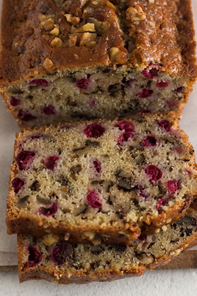 two slices of banana bread with cranberries and nuts on top, sitting next to each other