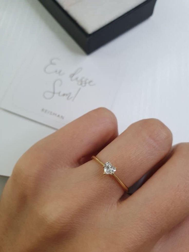 a woman's hand with a diamond ring on it and a box behind her