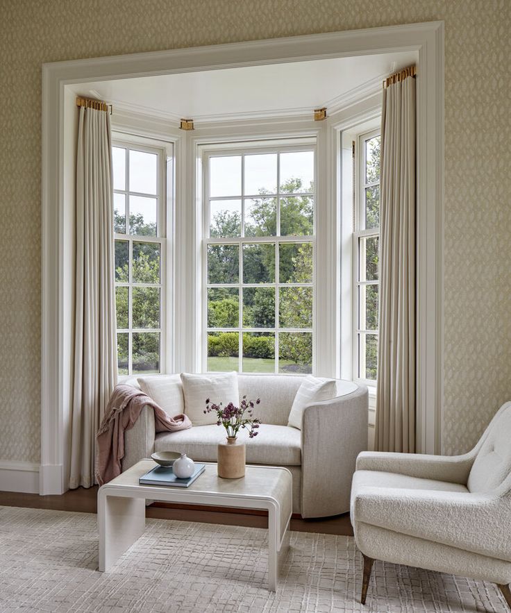 a living room filled with white furniture and large windows overlooking a lush green park area