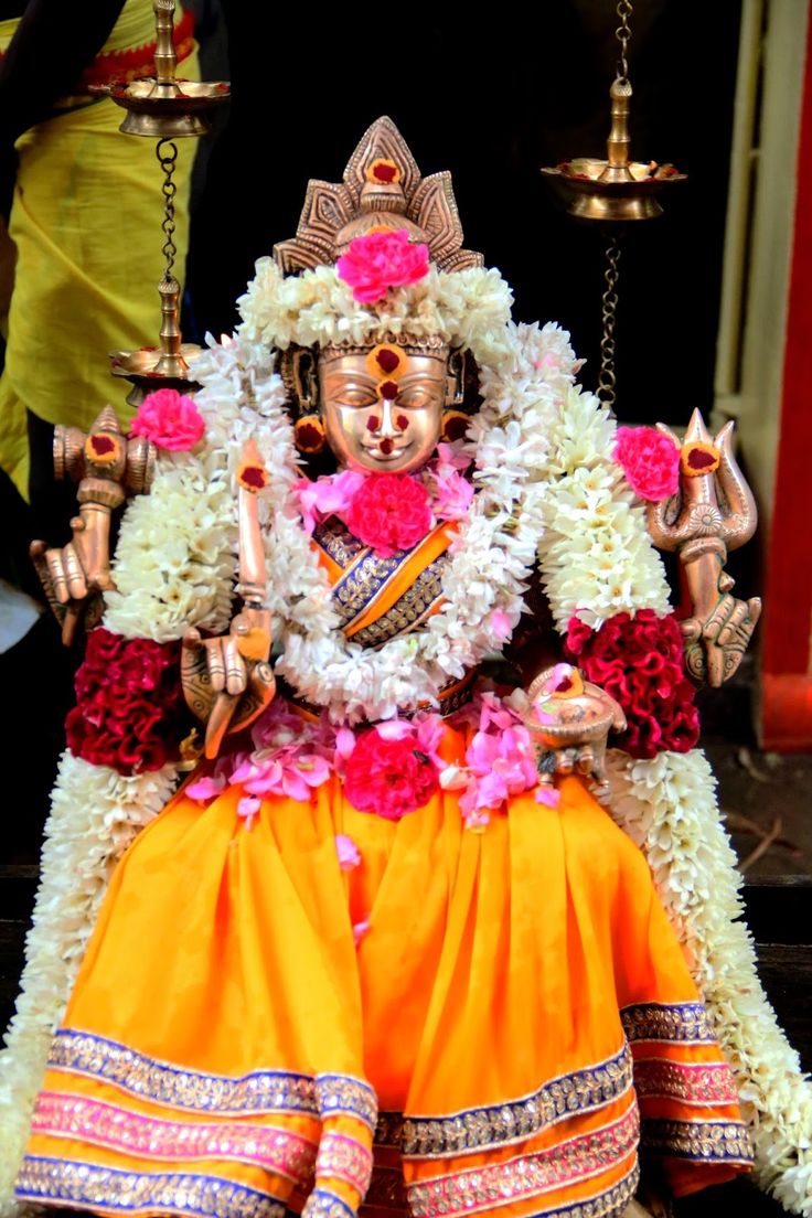 an idol sitting on top of a table with flowers around its body and hands in the air