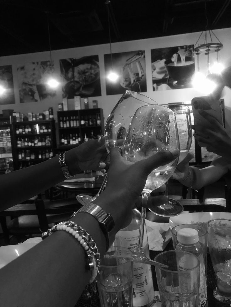 black and white photograph of two people holding wine glasses in front of each other at a bar