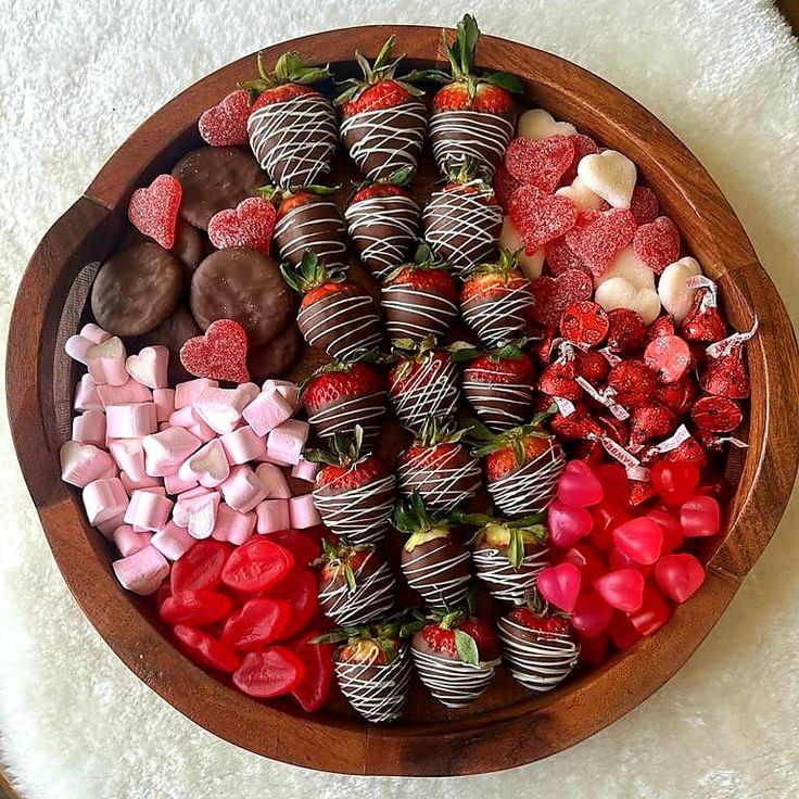 a wooden bowl filled with chocolate covered strawberries and other candys on top of a white rug