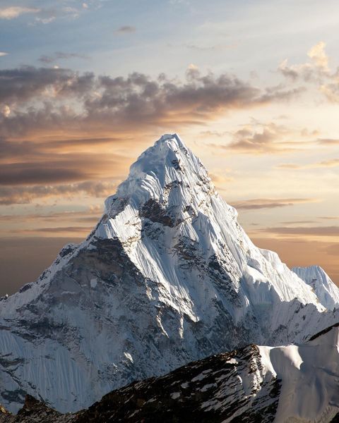 a large snow covered mountain with clouds in the sky and sun shining down on it