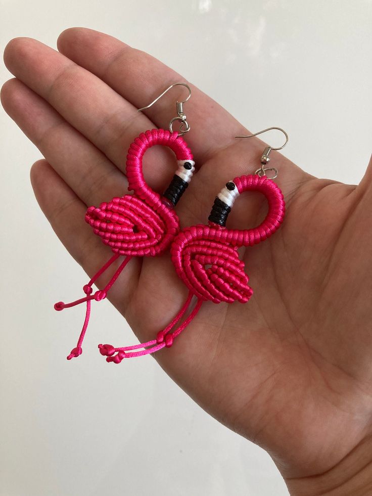 a pair of pink flamingo shaped earrings on a person's palm tree hand