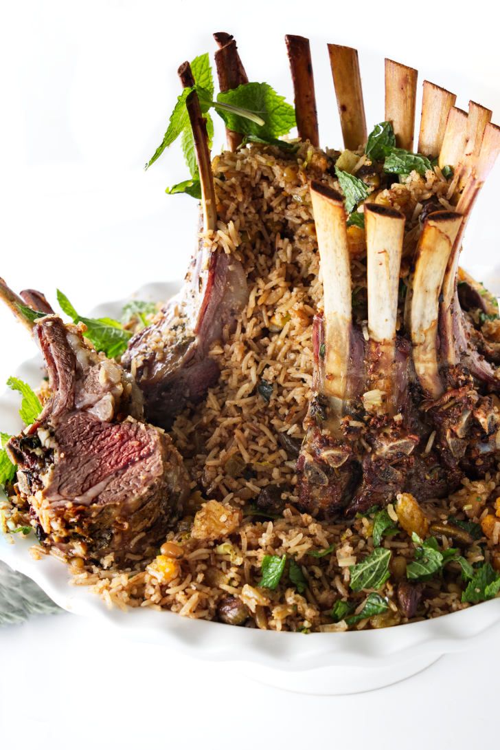 a white plate topped with meat and vegetables covered in rice, garnished with mint leaves