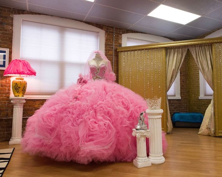 a pink dress sitting on top of a wooden floor in front of a lamp and window