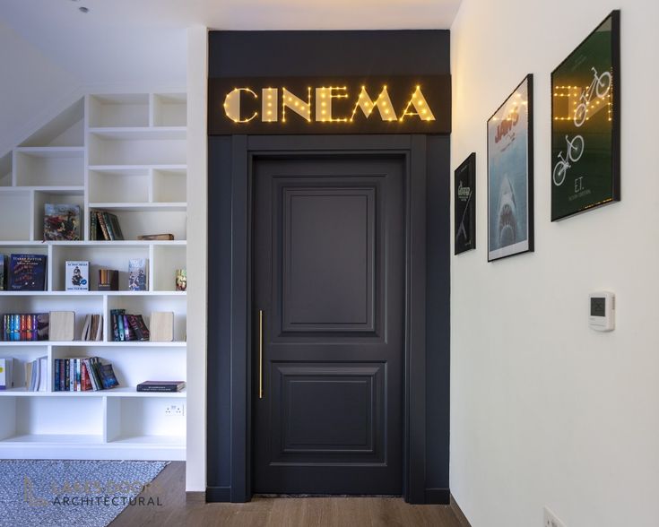 a black door with the word cinema lit up above it in front of bookshelves