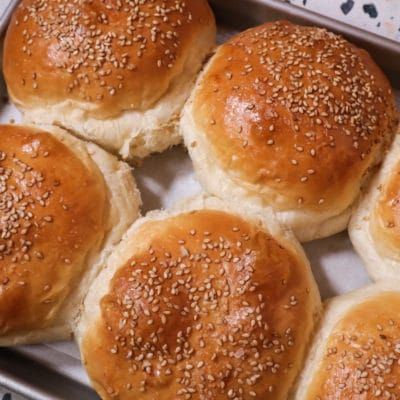 six buns with sesame seeds in a baking pan