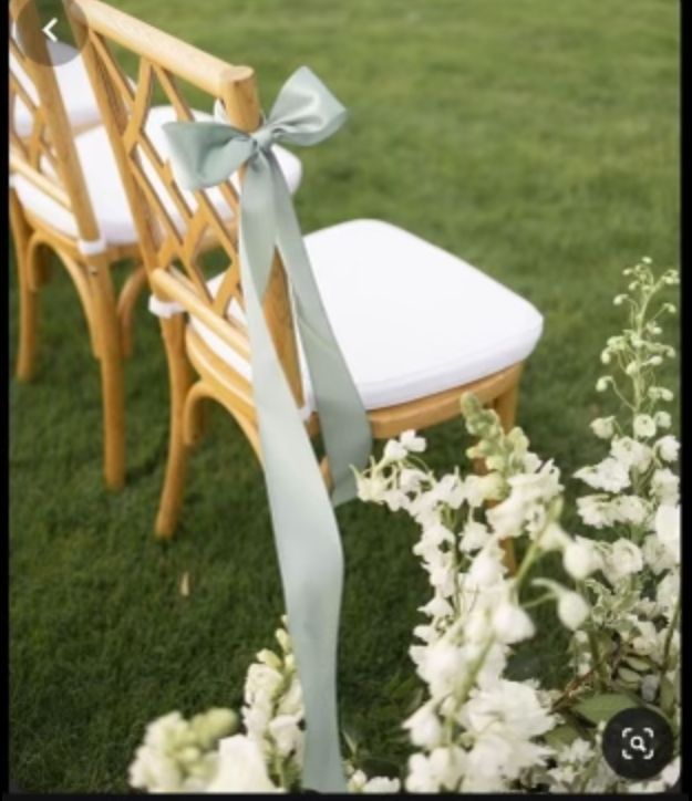 two wooden chairs with bows tied to them sitting in the grass next to some flowers