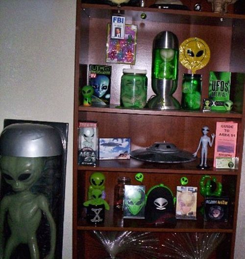 a book shelf filled with green alien figurines next to a wall mounted clock