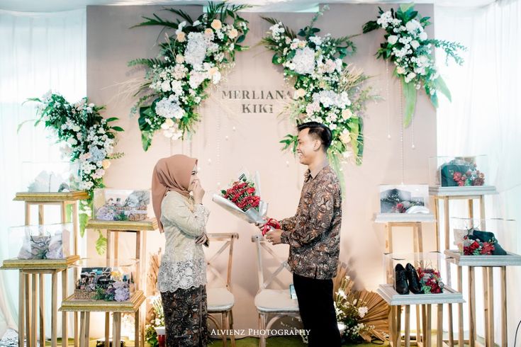 two people standing next to each other in front of a wall with flowers on it