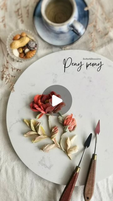 a white plate topped with flowers next to paintbrushes and a cup of coffee