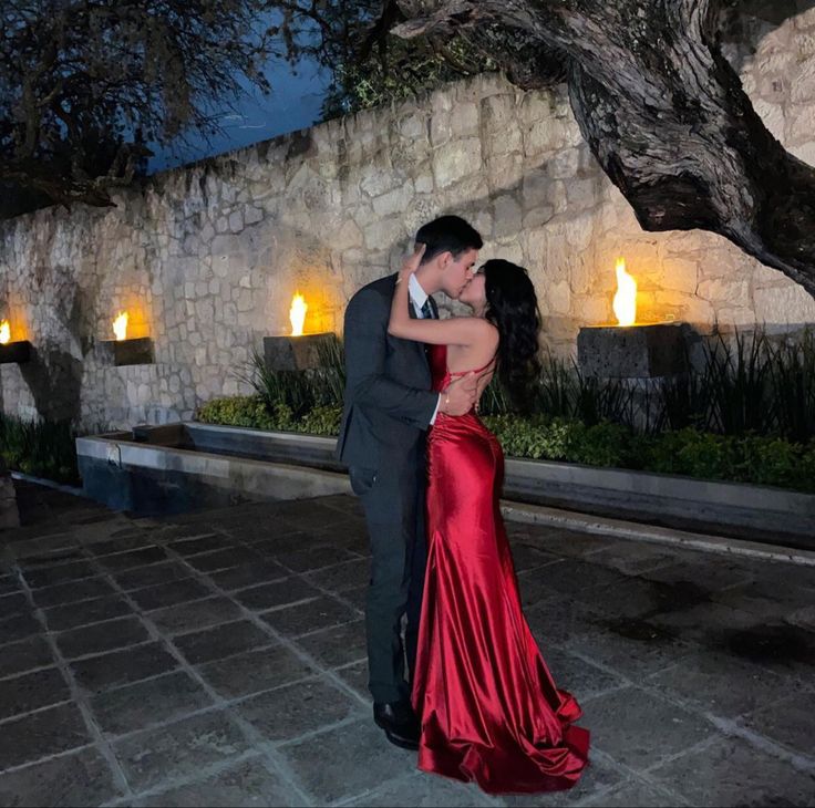 a man and woman dressed in formal wear dance together under a tree with lit candles behind them