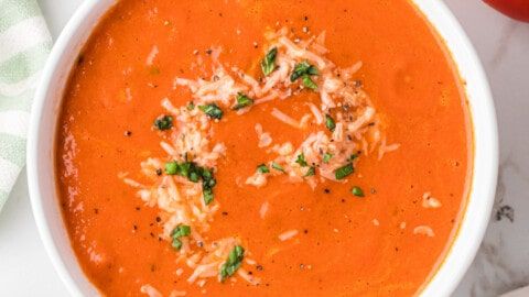 a bowl of tomato soup with parmesan cheese on top and an apple next to it