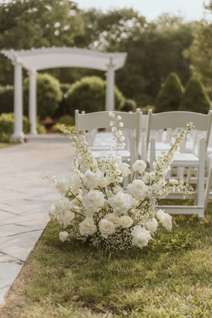 an outdoor ceremony set up with white chairs and flowers