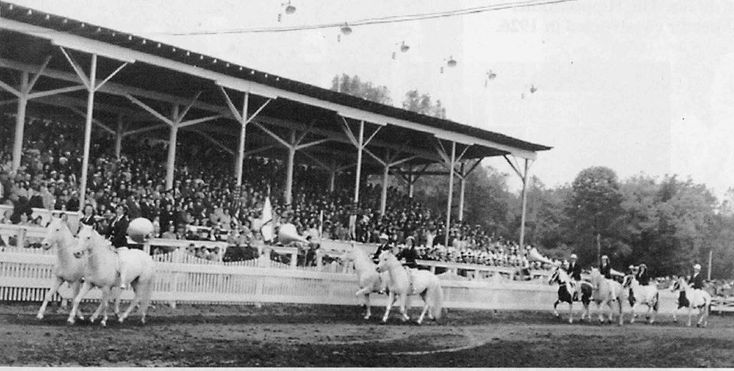 an old black and white photo of people on horses in front of a horse race