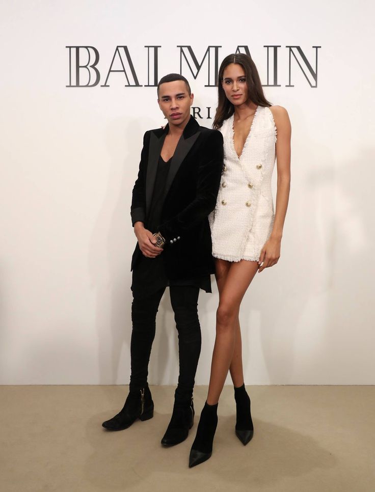 a man and woman standing next to each other in front of a wall with the words balmain on it