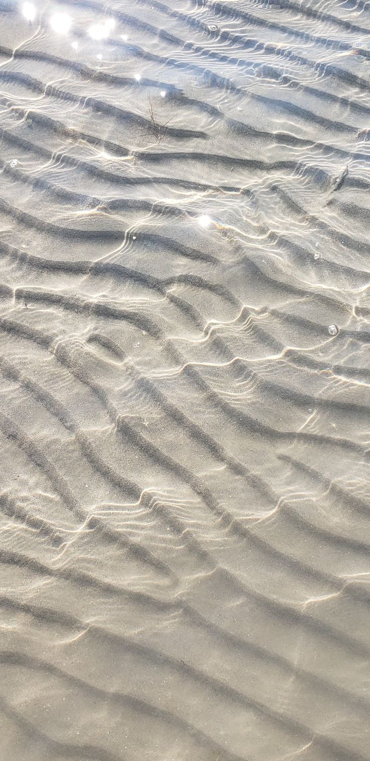 some sand and water on a beach with sun shining through the clouds in the background