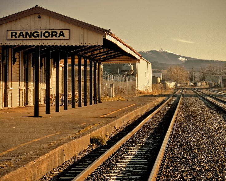 an old train station sits empty on the tracks next to some buildings and mountains in the background