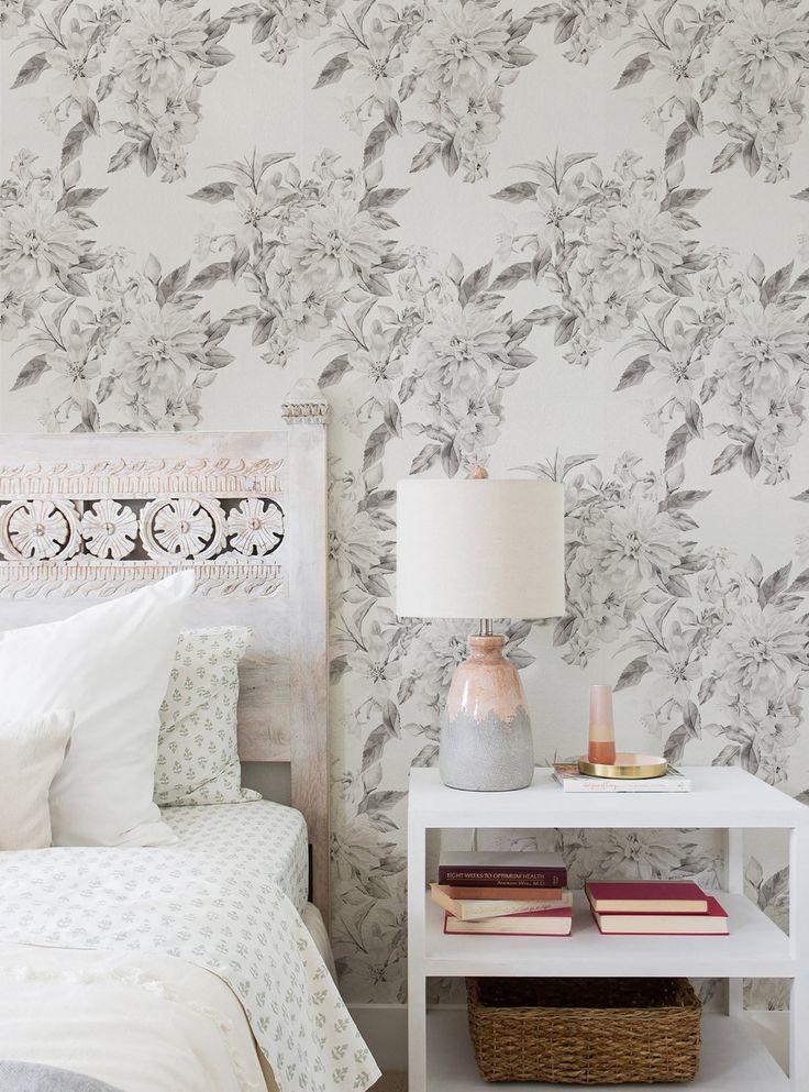 a white bed sitting next to a nightstand with a lamp on top of it in front of a floral wallpaper