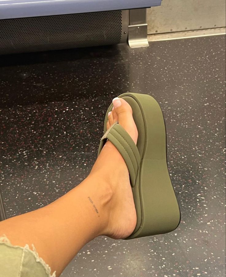 a woman's foot with a tattoo on her left leg and green shoes in front of an airport conveyor belt