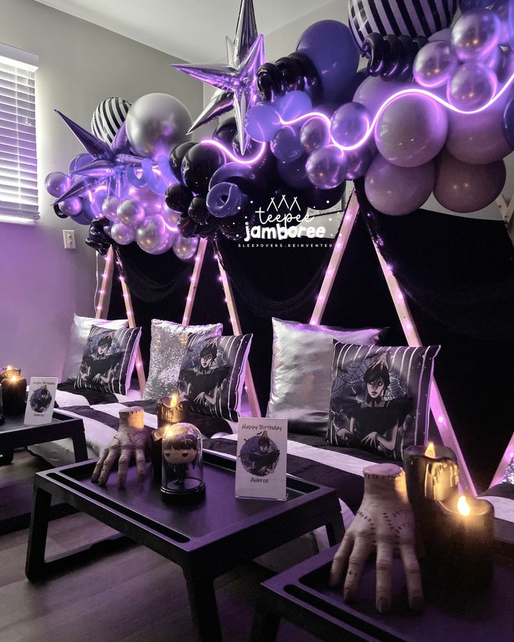 purple and black balloons are hanging from the ceiling in front of tables with candles on them