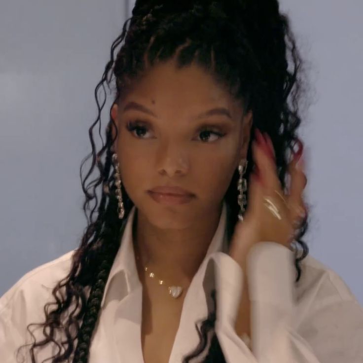 a close up of a person wearing earrings and a white shirt with long curly hair