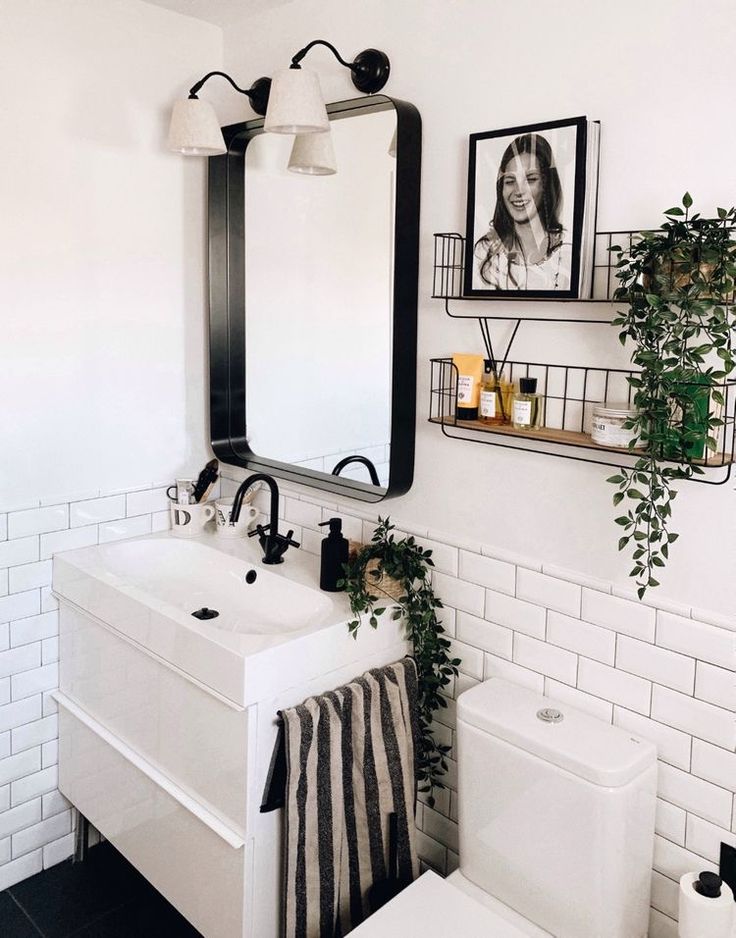 a bathroom with a sink, mirror and plants on the wall next to the toilet