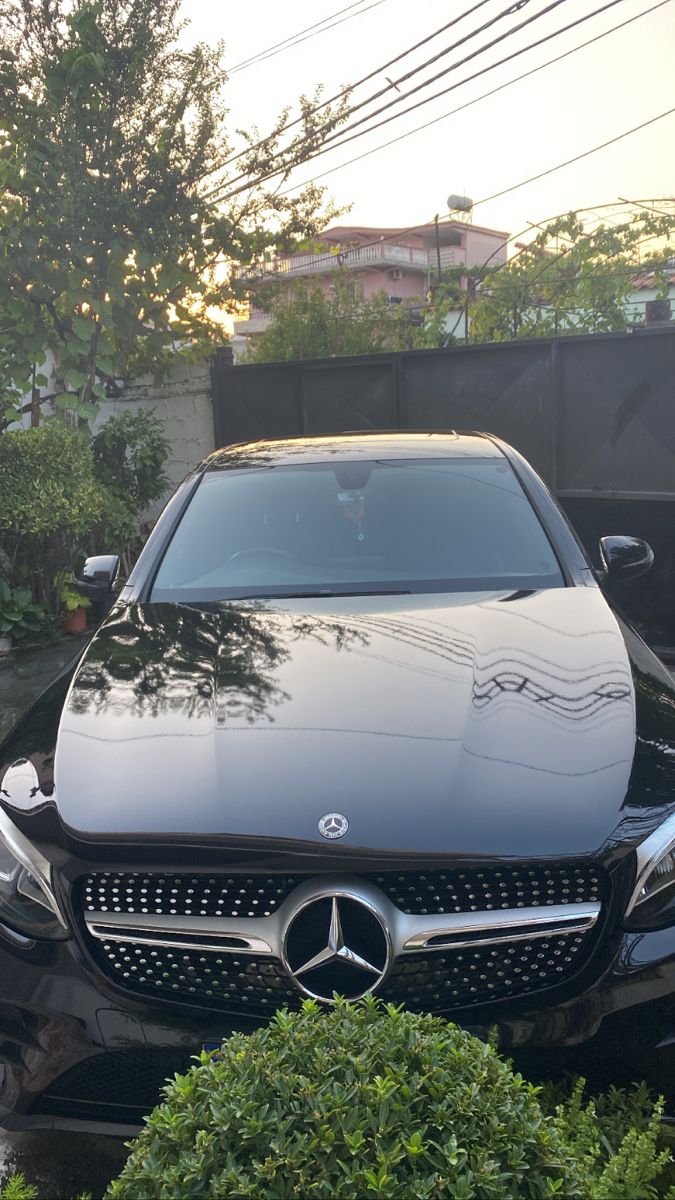 a black car parked in front of a house with trees and shrubbery around it