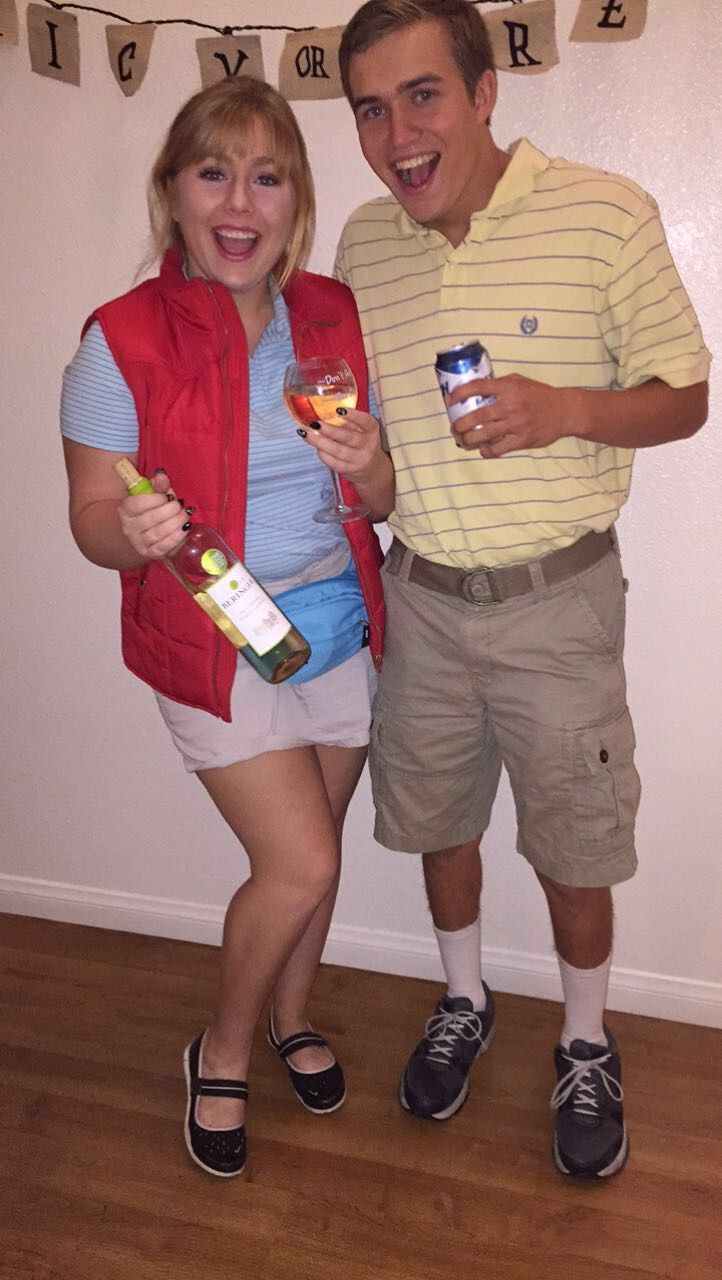 a man and woman standing next to each other holding wine glasses in front of a banner