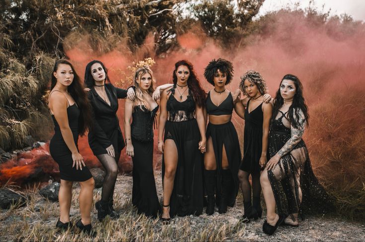 a group of women standing next to each other on top of a dirt field with trees in the background