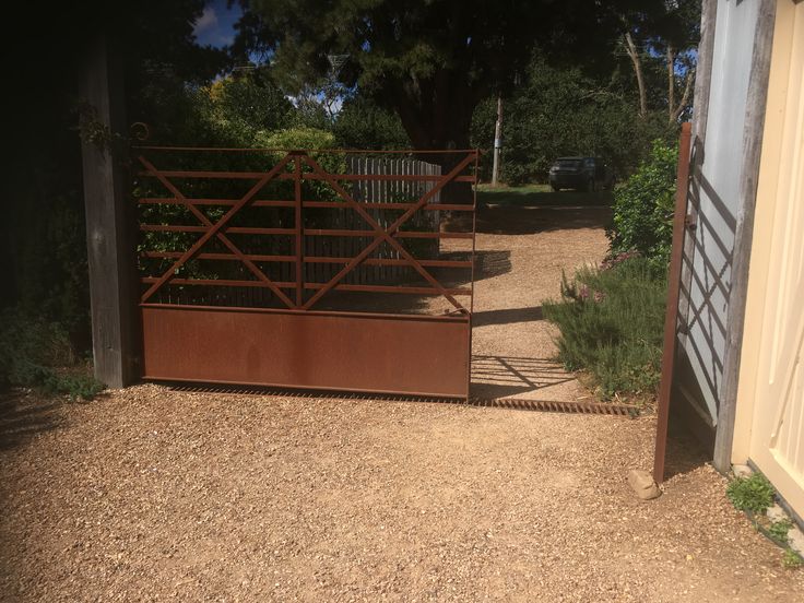 an open gate in the middle of a dirt area with trees and bushes behind it