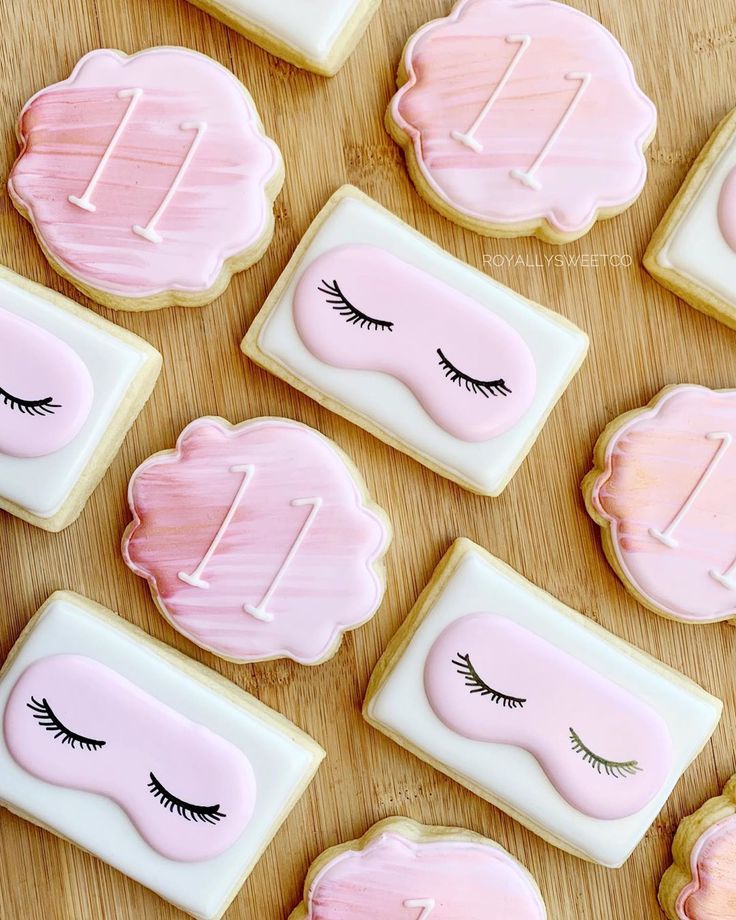 decorated cookies with pink icing and eyelashes are arranged next to each other on a wooden surface