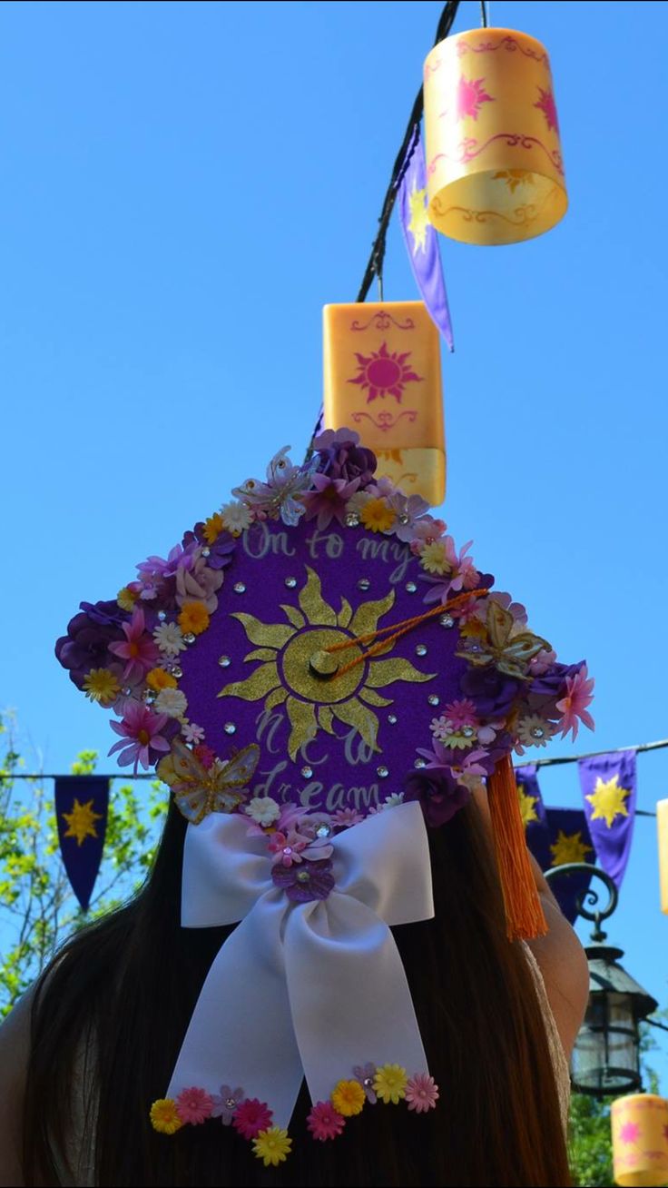 a woman wearing a purple hat with flowers on it's head and two candles hanging from the top