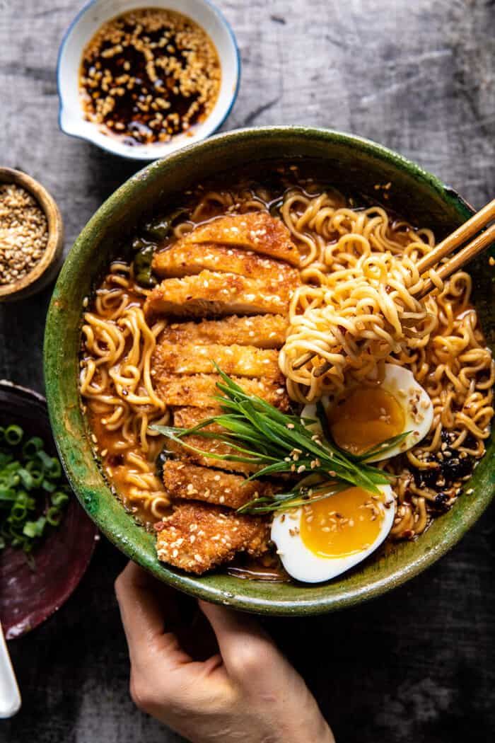 someone holding a bowl of ramen with chopsticks and an egg on top