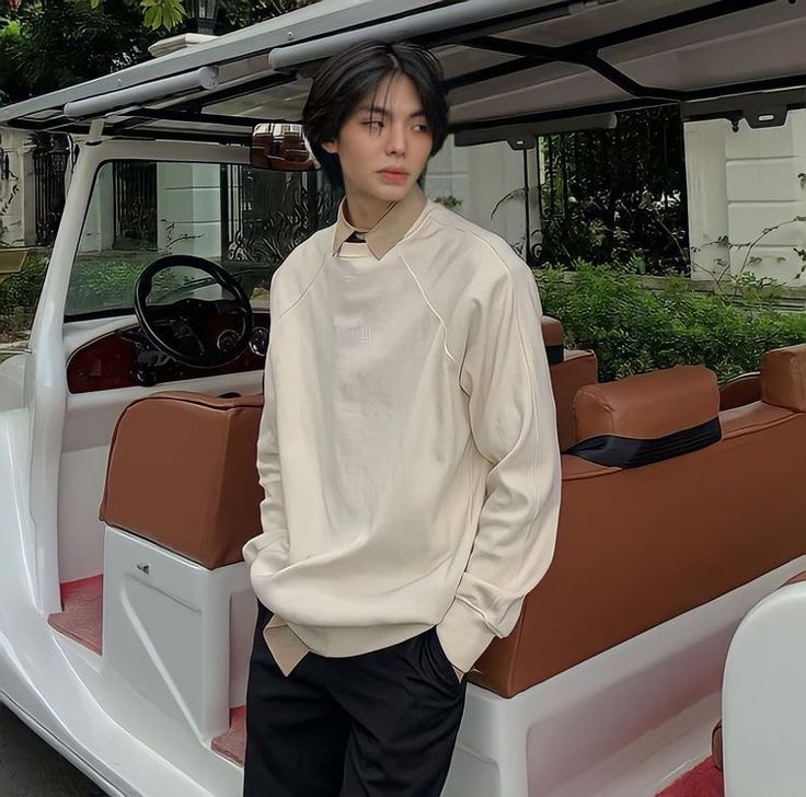 a young man standing next to a white and brown golf cart with his hands in his pockets