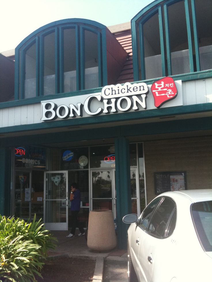 the front of a chicken restaurant with cars parked outside and people walking in the doorway