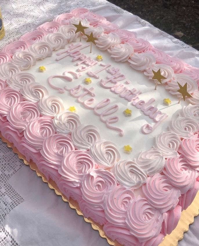 a pink and white birthday cake sitting on top of a table