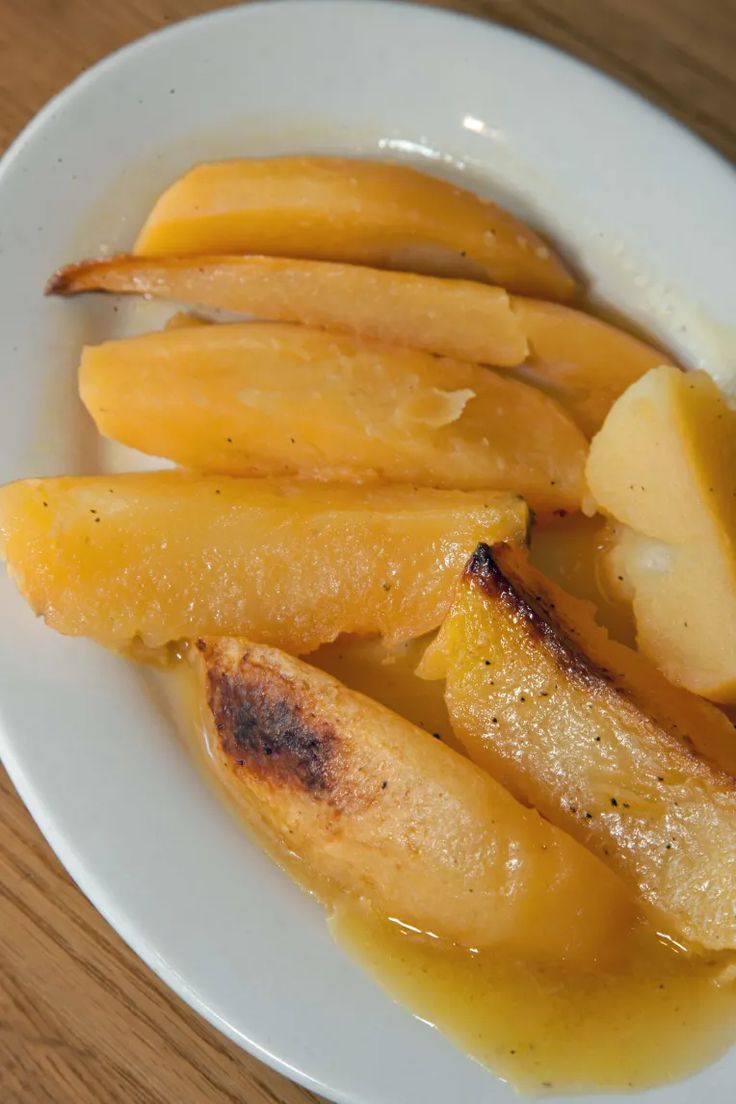 a white plate topped with sliced apples and gravy on top of a wooden table