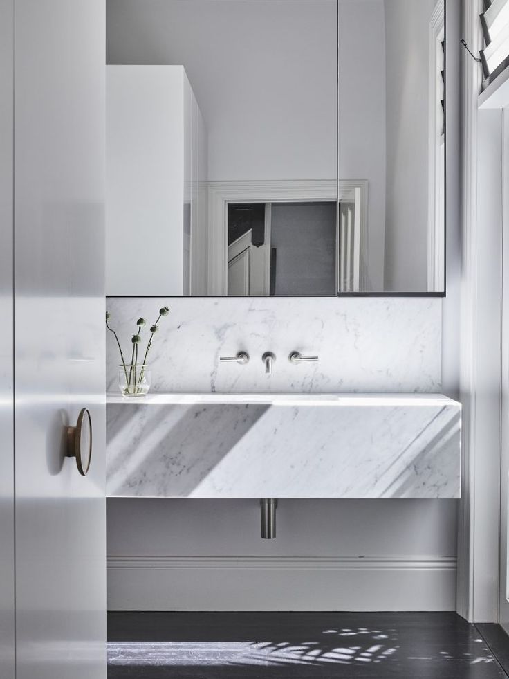 a white bathroom sink sitting under a mirror next to a window with sunlight coming in