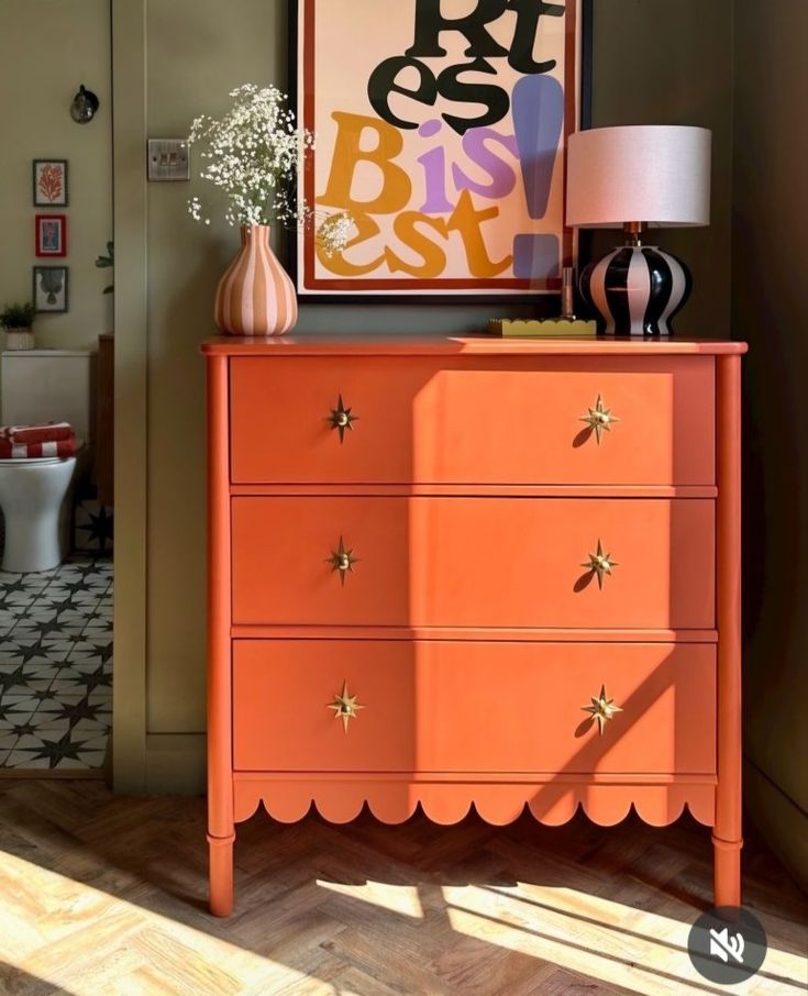 an orange dresser with gold stars on the drawers and a pink lamp next to it