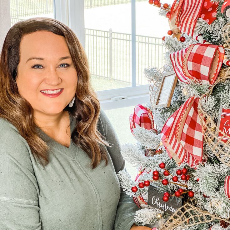 a woman standing in front of a christmas tree with red and white decorations on it