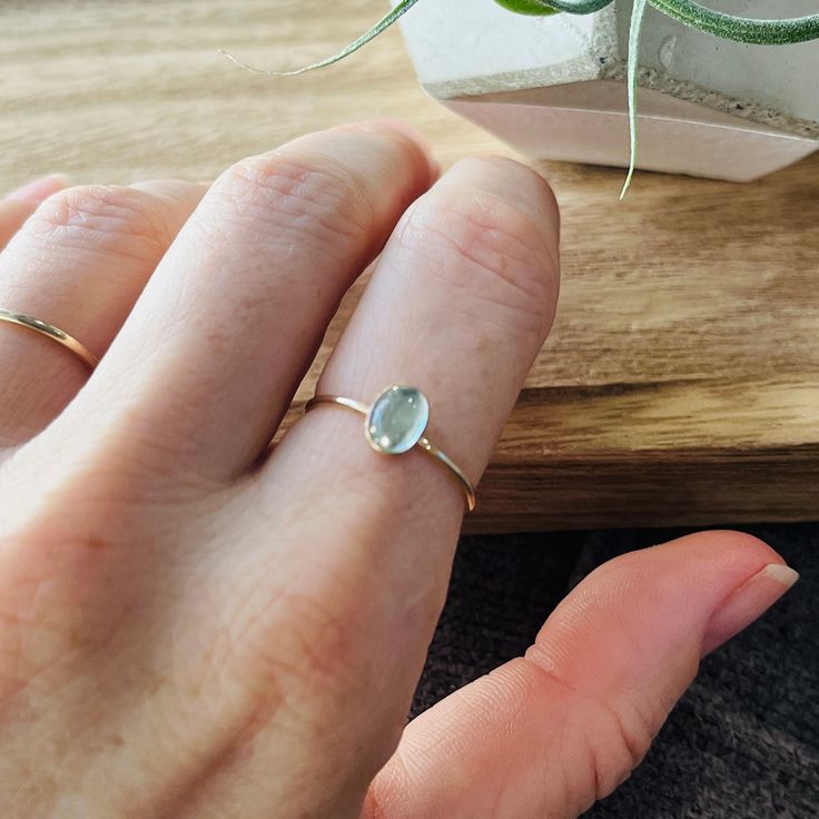 a person's hand with a ring on it and a plant in the background