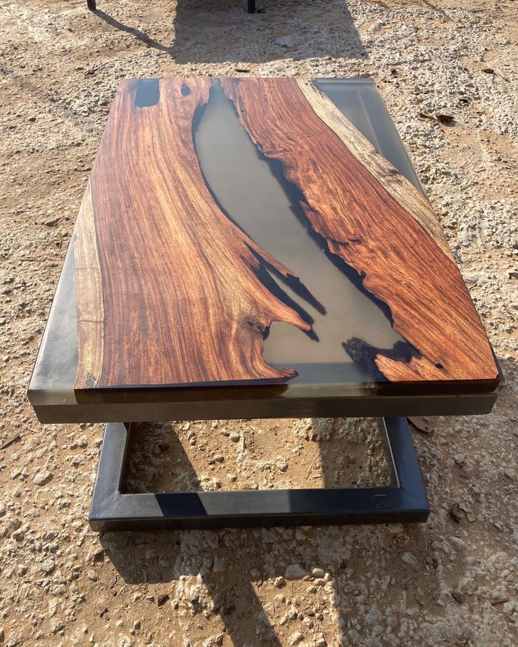 a wooden table sitting on top of a dirt ground next to a metal stand with water in it